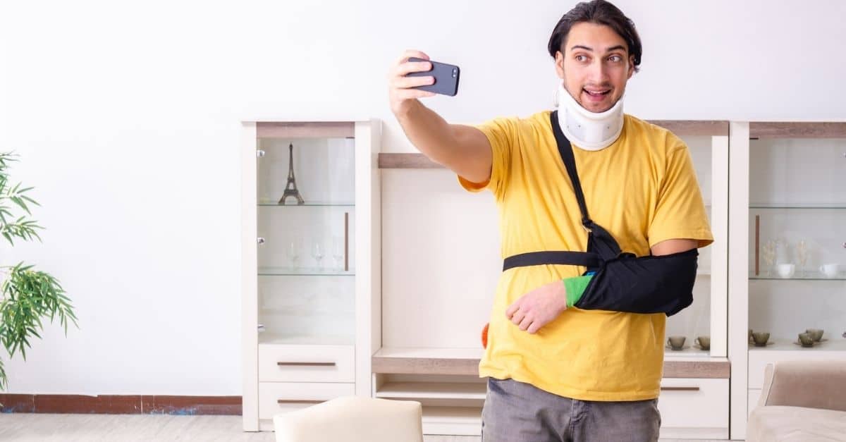 Young man with a broken arm using his phone with one hand.