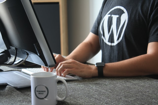 A person in a WordPress tee shirt typing at a keyboard with a monitor in front of them